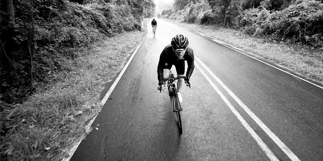 Rennradfahrer trainiert auf einer Landstraße durch den Wald während einer intensiven Radtour.