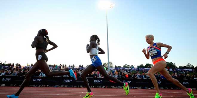 Athletinnen sprinten während eines Leichtathletikrennens auf der Laufbahn vor Publikum im Stadion.