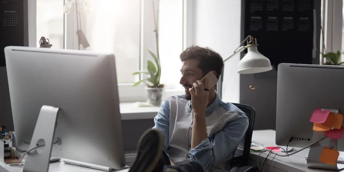 Junger Student telefoniert während er am Computer arbeitet