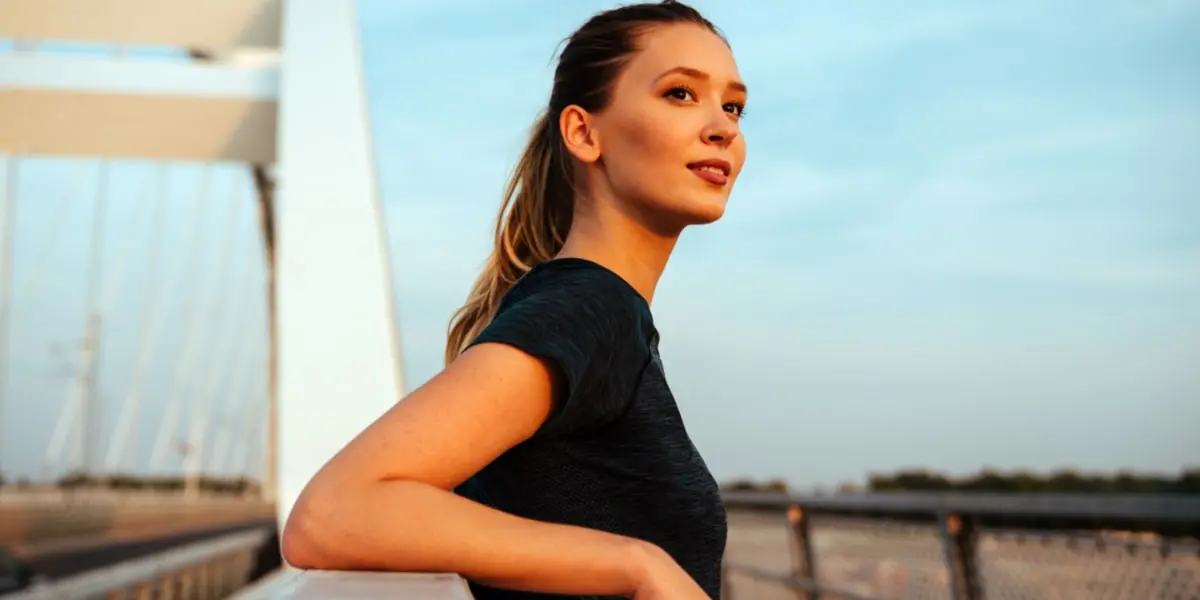 Chica joven mirando el horizonte apoyada en la valla de un puente Chica joven mirando el horizonte apoyada en la valla de un puente