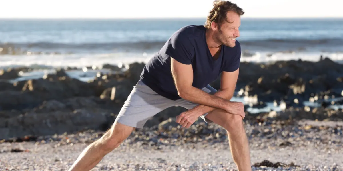 Hombre deportista estirando en la playa Hombre deportista estirando en la playa