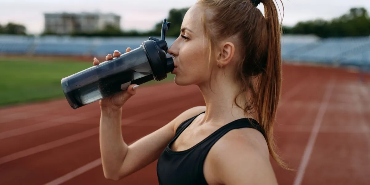 Corredora hidratándose correctamente antes de correr en la pista para prevenir la hematuria Corredora hidratándose correctamente antes de correr en la pista para prevenir la hematuria