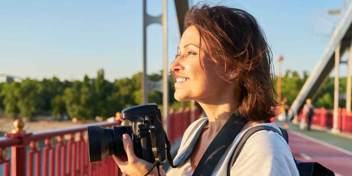 Mujer fotógrafa relajándose viendo el atardecer mientras saca fotos con una cámara profesional