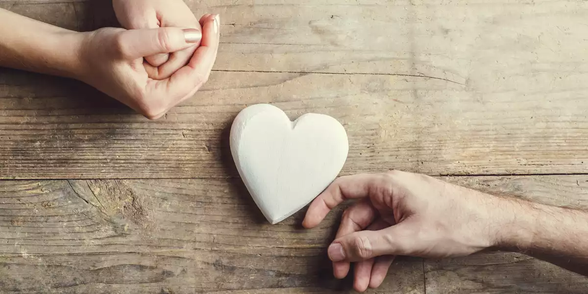 Hände auf Tisch, die ein Herz aus Holz berühren Hände auf Tisch, die ein Herz aus Holz berühren