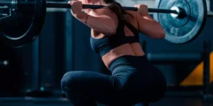 Chica haciendo sentadilla con peso en el gimnasio